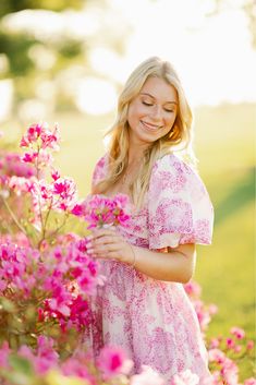 a beautiful blonde woman in a pink dress standing by some flowers