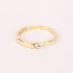 a yellow gold ring with a single diamond on the top and bottom, sitting on a white surface