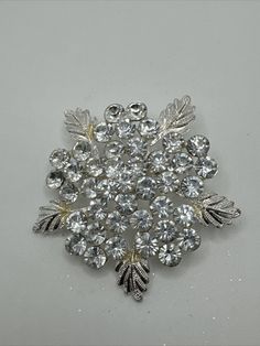 This beautiful vintage brooch features a stunning dimensional snowflake design with intricate details that are sure to catch the eye. The brooch is crafted from silver-tone metal and adorned with sparkling crystal stones. It is signed and in its original condition, with no modifications or repairs. The brooch is a unique piece of fashion jewelry from an unknown origin, but it is believed to have been made in the United States. The snowflake design is perfect for winter events or as a statement p Sparkling Silver Brooch For Anniversary, Silver Sparkling Brooch For Anniversary, Silver Sparkling Brooches For Anniversary, Luxury Silver Brooch With Intricate Design, Silver Crystal Brooch Pin, Elegant Crystal Brooches With Sparkling Stones, Luxury Elegant Star-shaped Brooches, Winter Event, Silver Flower-shaped Brooches With Rhinestones