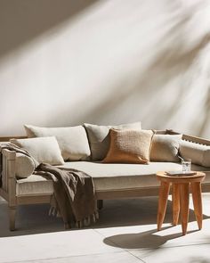 a living room with a couch, table and pillows on the back side in front of a white wall