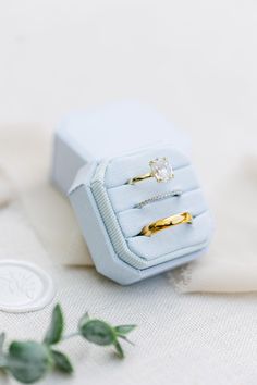 two gold wedding rings sitting in a blue ring box on top of a white cloth