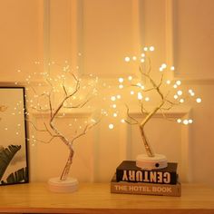 two small trees with white lights on top of a wooden table next to a book