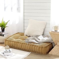 a bed that has some books on it and a plant in the corner next to it