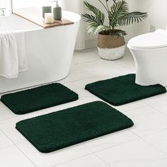 three green bathroom rugs in front of a white bathtub and toilet with plants