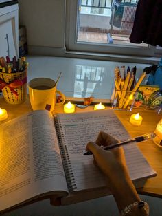 a person is writing in a book with candles around them