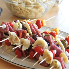 several skewered meats and vegetables are on a plate next to bowls of fruit