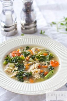 a white plate topped with chicken and veggie soup next to silver spoons