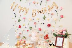 a birthday cake and dessert table with flowers on the wall in front of it that says happy birthday