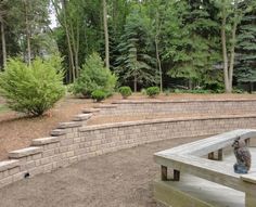 a cat sitting on top of a wooden bench next to a stone wall and trees