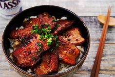 a bowl filled with meat and rice next to chopsticks on a wooden table