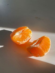 two peeled oranges sitting on top of a white counter next to a shadow from the sun