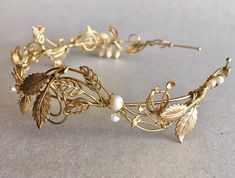 a gold headband with leaves and pearls on the side, sitting on a table