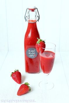 two strawberries are next to a bottle of strawberry juice and a glass with the liquid in it