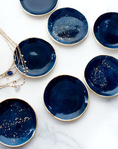 six blue plates with gold speckles are arranged on a white table top and one has a necklace hanging from it