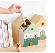 a child's hand holding a pencil near a toy house