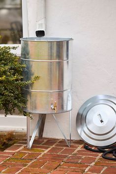 a large metal container sitting on top of a brick floor next to a potted plant