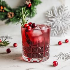 a red drink with cranberries and rosemary garnish in a glass on a table