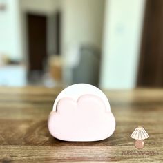 a pink cloud shaped object sitting on top of a wooden table next to a lamp