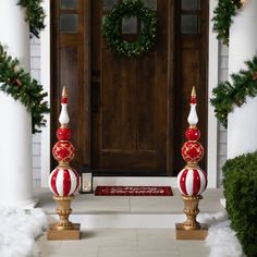 two red and white christmas decorations in front of a door with wreaths on it