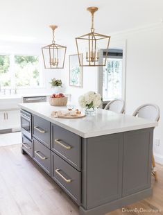 a kitchen island with marble counter tops and gold pendant lights hanging from it's ceiling