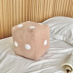 a pink dice pillow sitting on top of a bed next to a rolled up newspaper