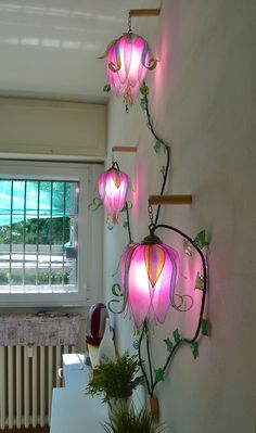 three pink lights hanging from the side of a wall next to a potted plant