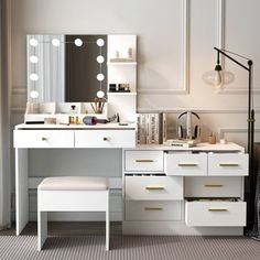 a white vanity with drawers and lights on the top shelf next to a mirror, stool and lamp