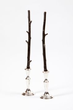 two silver candlesticks with twig stems on each one, set against a white background