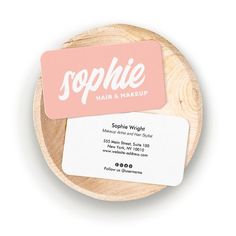 a pink business card sitting on top of a wooden plate next to a white business card