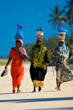 three women walking down the beach carrying bags on their heads