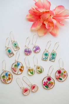 a bunch of earrings sitting on top of a white table next to a pink flower