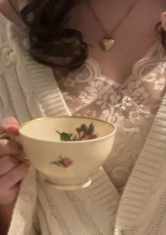 a woman in white sweater holding a bowl with flowers on it and looking at the camera