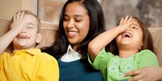 a woman sitting next to two children on a couch with their hands in the air