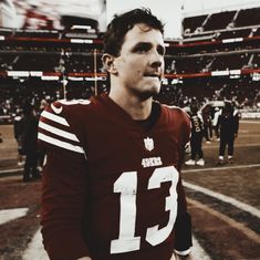 a man standing on top of a football field wearing a jersey with the number 13 on it