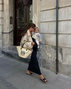 a woman carrying a baby in her arms while walking down the street next to a building