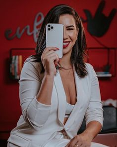 a woman taking a selfie with her cell phone while sitting on a table in front of a red wall