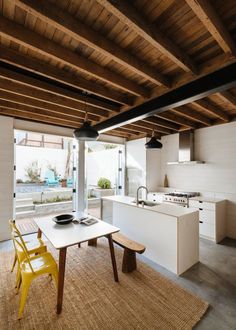 an open kitchen and dining area with wooden beams on the ceiling, along with yellow chairs