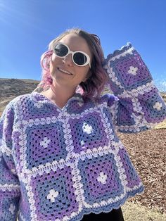 a woman wearing sunglasses and a crocheted granny's sweater is posing for the camera