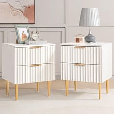 two white nightstands sitting next to each other in front of a painting on the wall