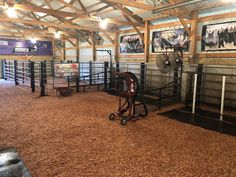 the inside of a barn with several stalls and horses in pens, hay on the floor