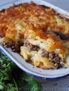 a casserole dish with meat and cheese in it on a plate next to greens