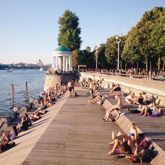 many people are sitting on the dock by the water and some have sunbathers