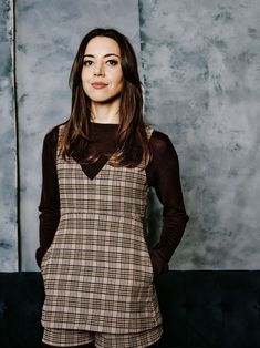 a woman standing in front of a wall with her hands on her hips and looking at the camera