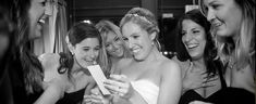 a group of women standing next to each other in front of a mirror looking at a cell phone