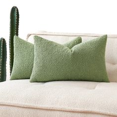 two green pillows sitting on top of a couch next to a cacti plant