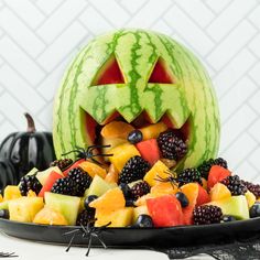 a watermelon carved to look like a jack - o'- lantern surrounded by fruit