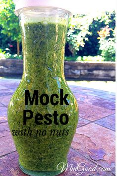 a glass jar filled with green pest sitting on top of a stone floor next to trees