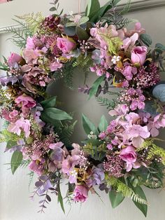 a wreath with purple flowers and greenery is hanging on the front door to welcome guests