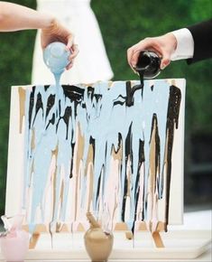 two people are painting on an easel with blue and black paint, while one person is holding a bottle