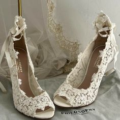 a pair of white high heeled shoes with lace and bows on the heels are next to a gold umbrella